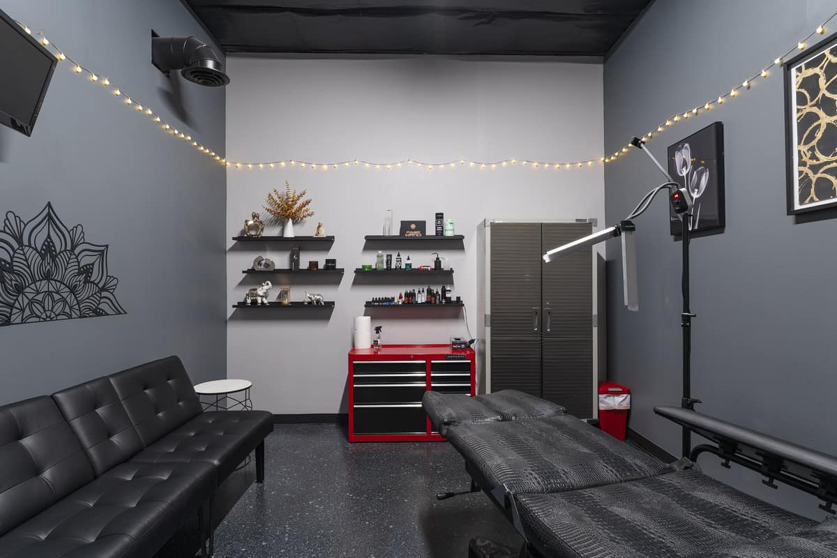 A grey suite with a client couch, shelves, a red tool chest and a tattoo bed